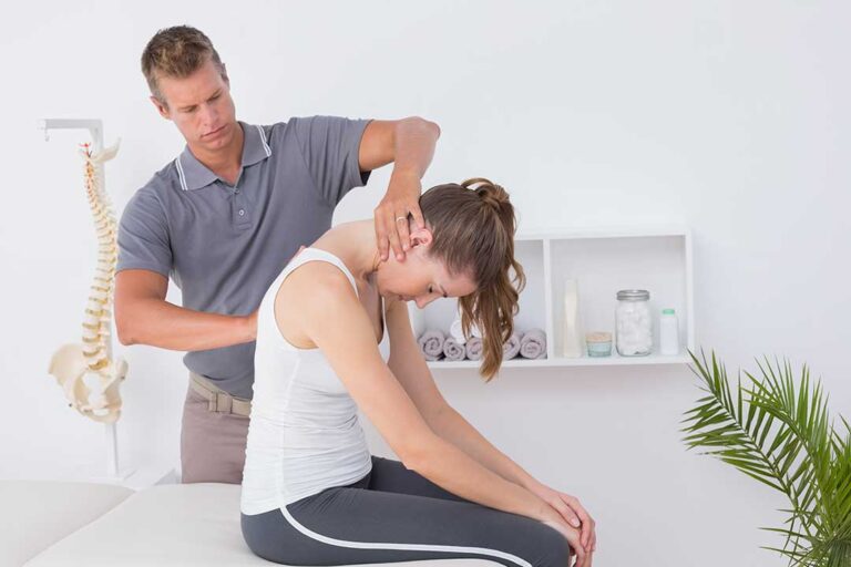 A chiropractor assessing an athlete’s knee on a padded examination table in a bright clinical setting.